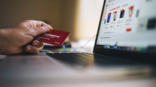 Person Holding Red Credit Card in Front of Laptop - Shopping Website